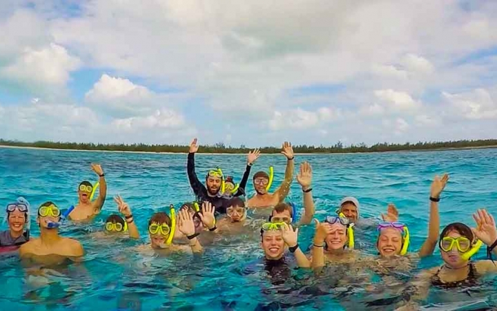 a group of gap year students wearing snorkles stand in blue water and raise their hands in celebration 